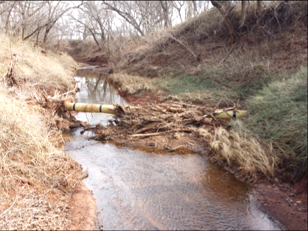 Before: An exposed line in a creek crossing choked with debris